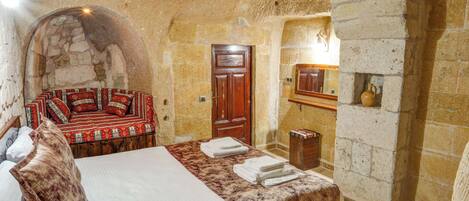 A traditional stone-walled room with a bed, a wooden door, and a small wooden cabinet.