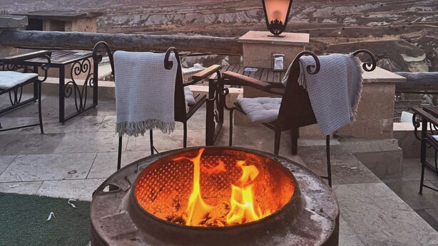 Un patio con un hogar de fuego, mobiliario exterior y vistas a la puesta de sol sobre un paisaje urbano.