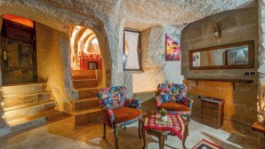 Un interior rústico de piedra con chimenea, dos sillones con estampado y una escalera que conduce a una habitación acogedora.
