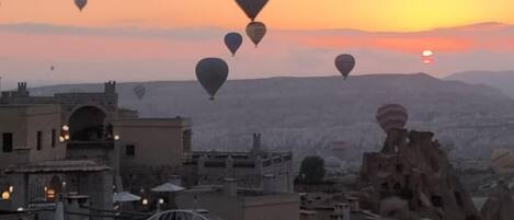 A rooftop terrace with outdoor seating, a view of the sunset, and multiple hot air balloons in the sky.