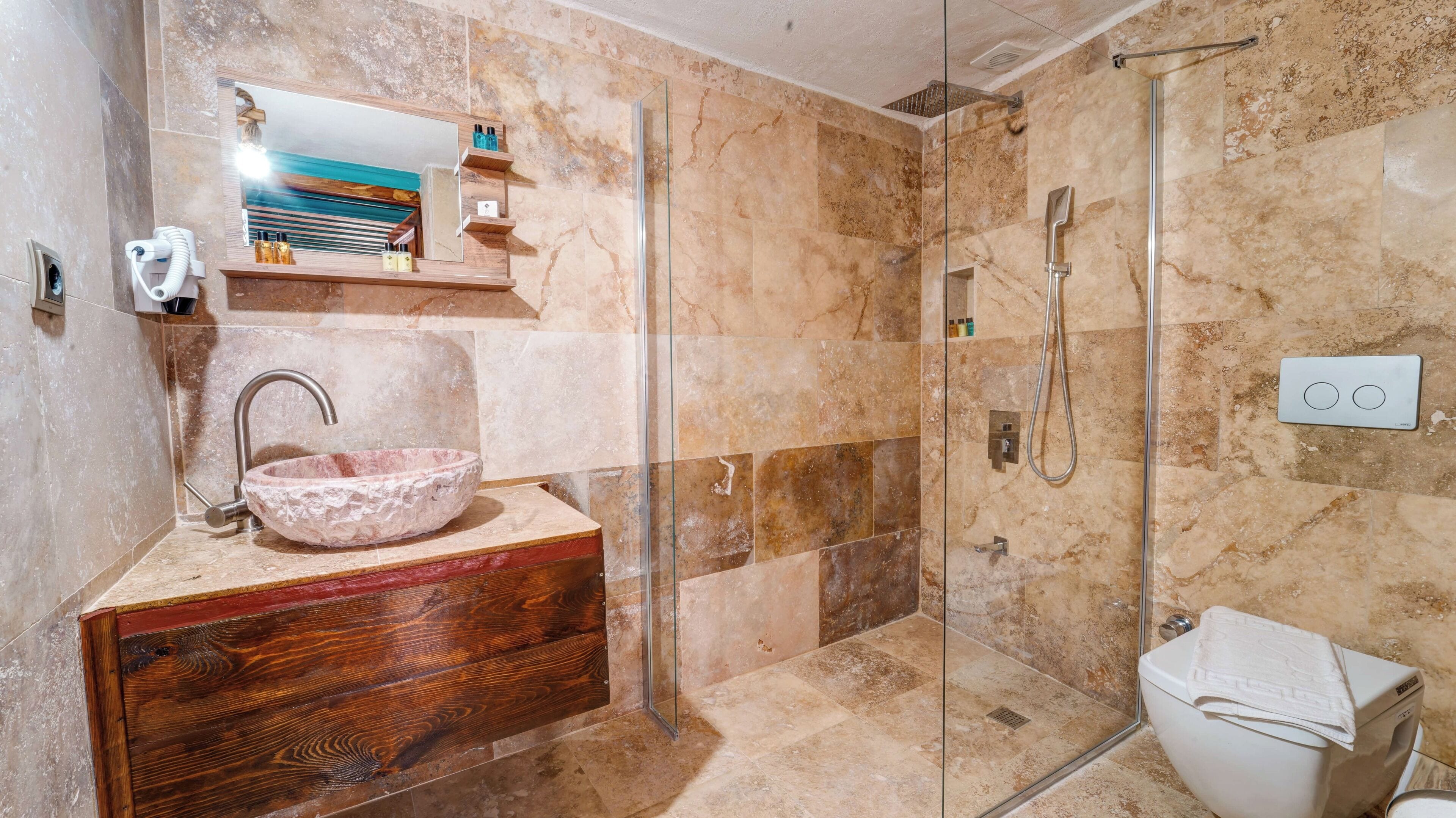 Un baño con lavamanos de mármol, tocador de madera, cabina de ducha de vidrio y un inodoro.