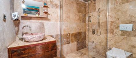 Un baño con lavamanos de mármol, tocador de madera, cabina de ducha de vidrio y un inodoro.