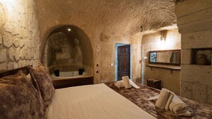 Un dormitorio rústico con paredes de piedra, una cama, cabecera de madera, un espejo grande y un lavabo.