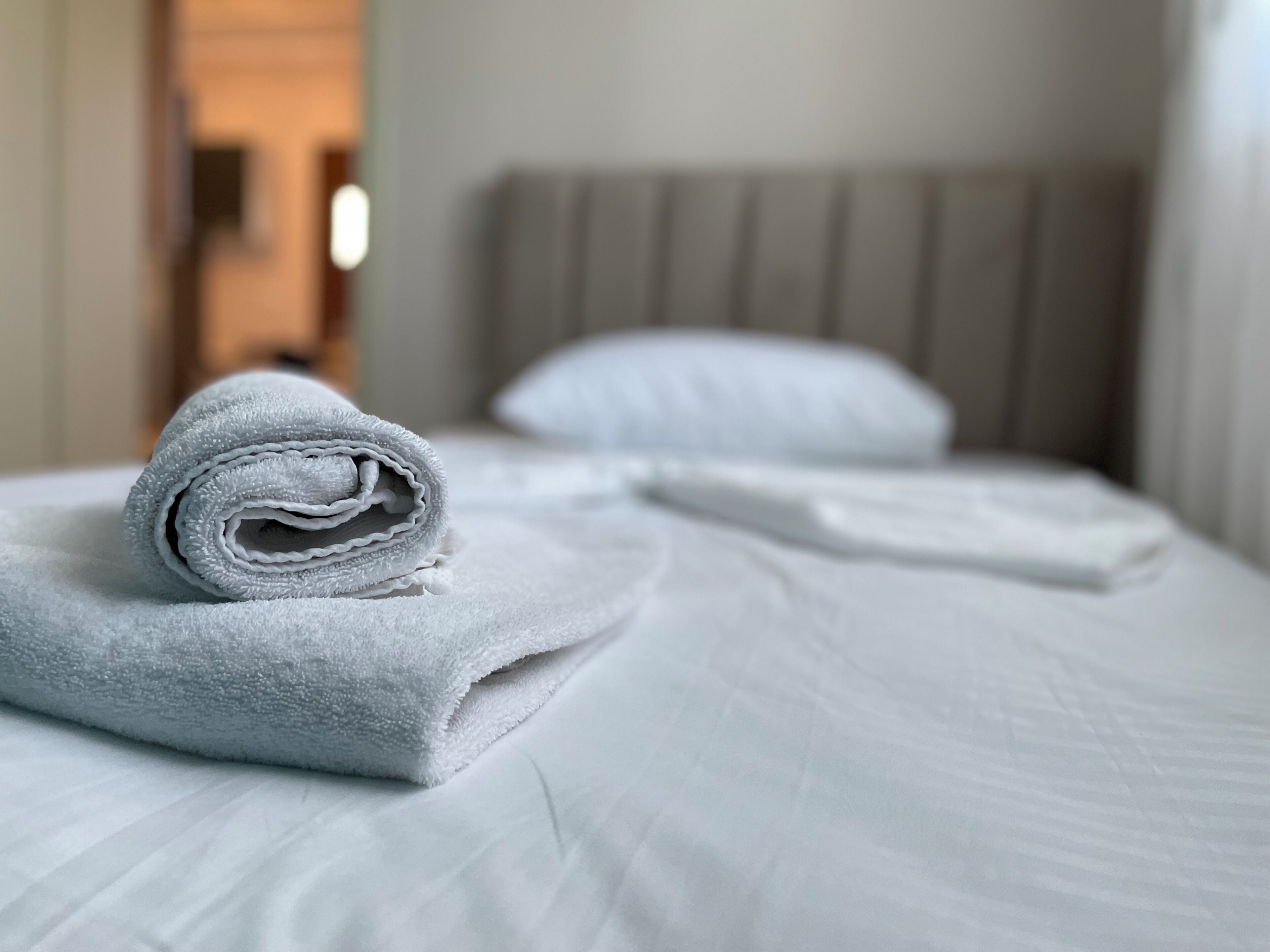 Ein ordentlich gemachtes Bett mit einem zusammengerollten Handtuch und einem Kopfkissen.