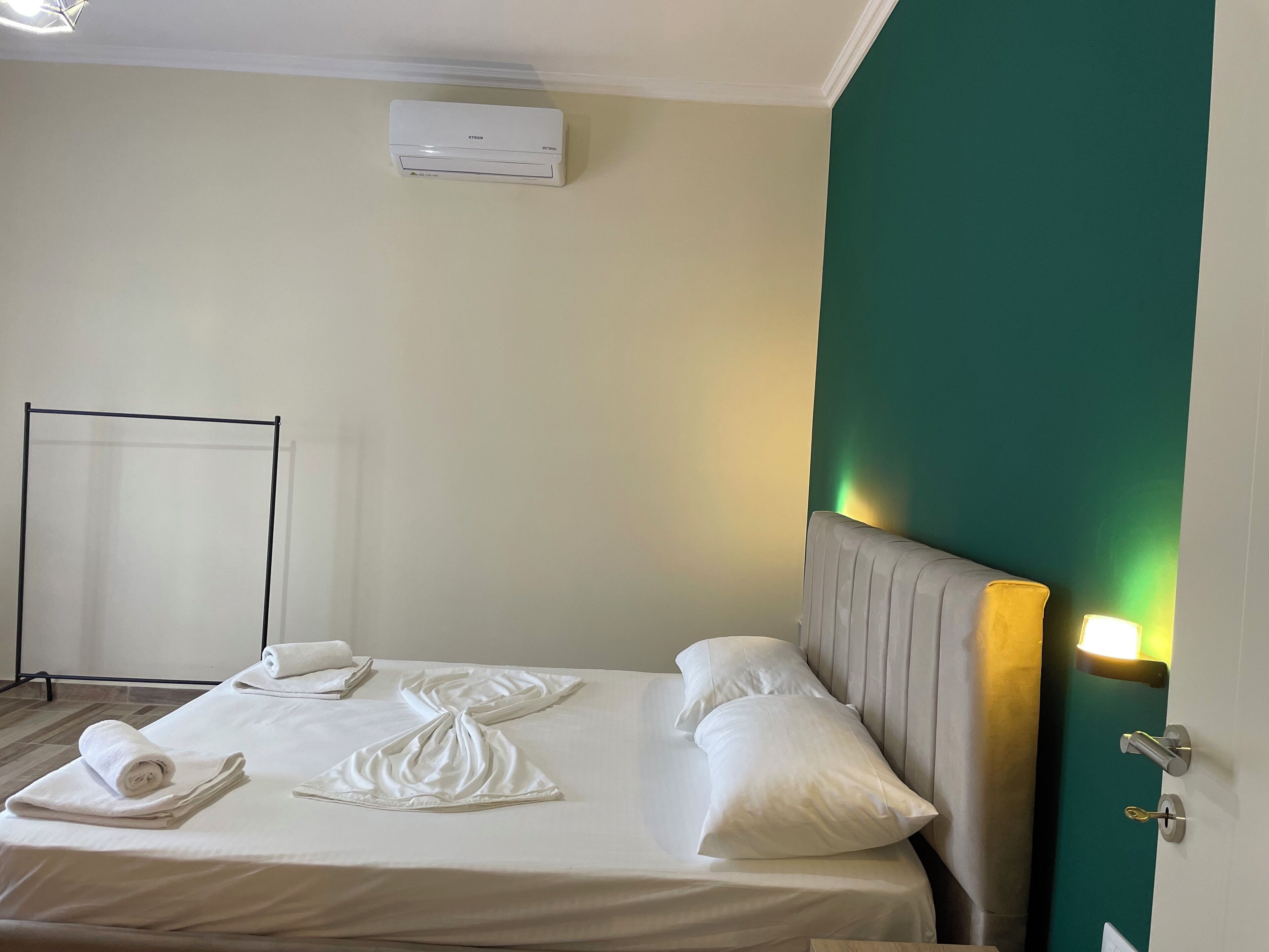A hotel room with a bed, pillows, a rolled towel, a standing heater, and a wall-mounted air conditioner.
