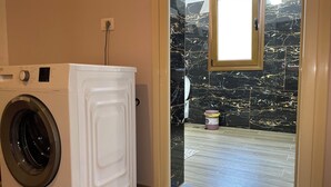 A laundry room with a front-loading washing machine, a small window, and a marble-patterned wall.