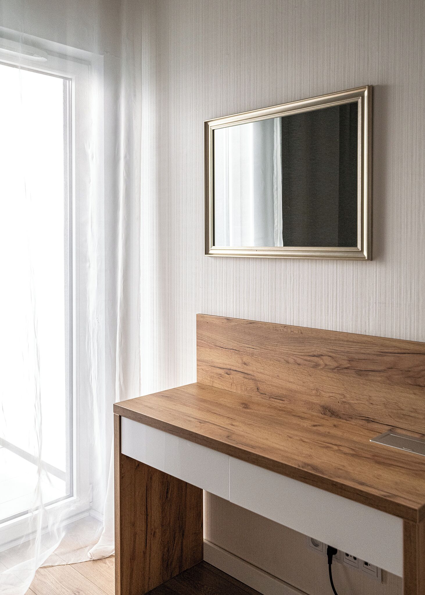 Ein Badezimmer mit Waschtisch aus Holz, einem Spiegel und einem Fenster mit durchsichtigen Vorhängen.