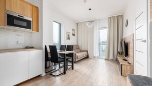 A modern kitchen with white cabinets, a built-in oven, and a dining area with a table and chairs. - RentPlanet - Bliska Wola (Warsaw)