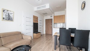 A modern living room with a sofa, a coffee table, and a dining area with chairs and a table. - RentPlanet - Bliska Wola (Warsaw)