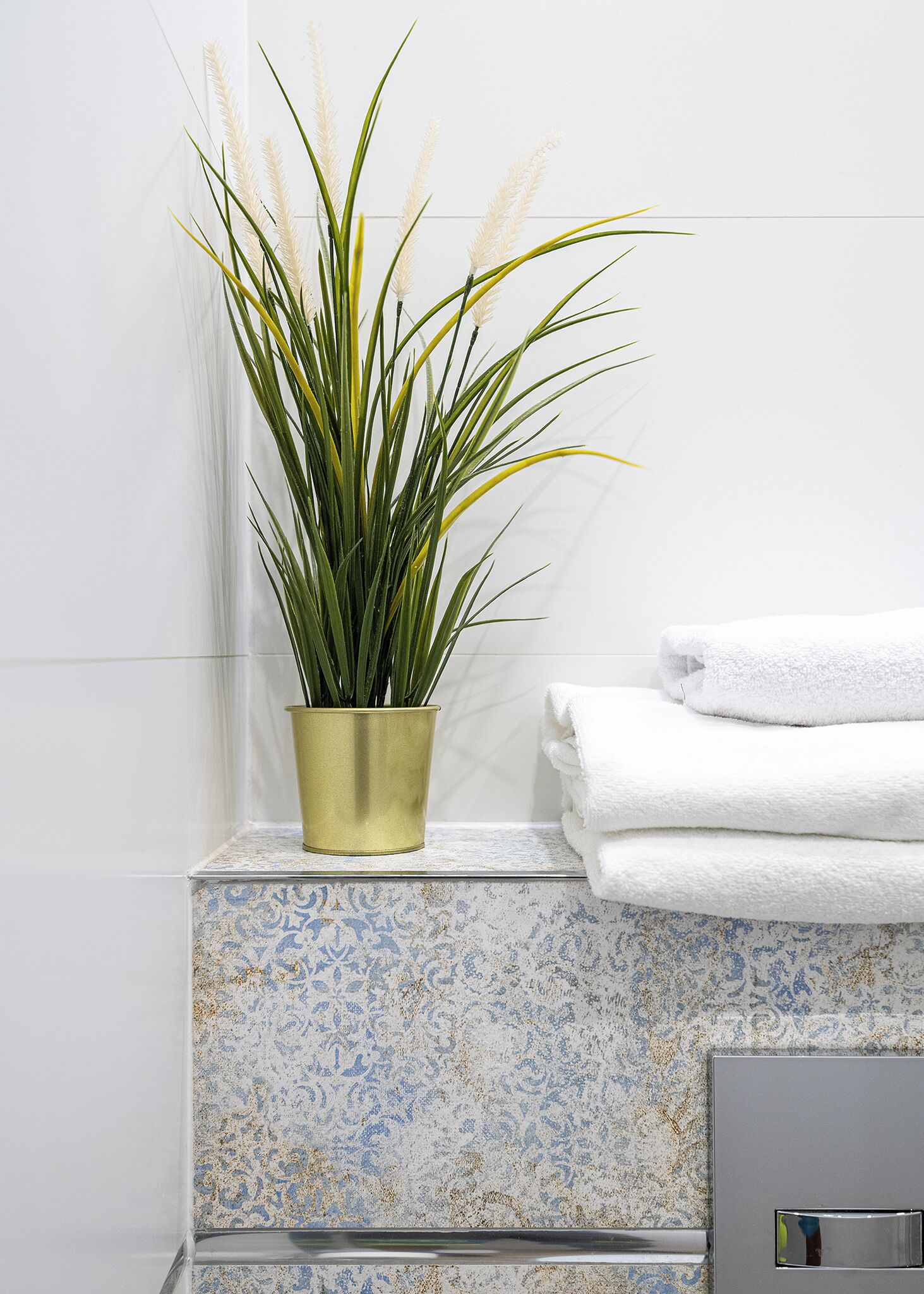 Une salle de bain avec une plante en pot, des serviettes blanches et un mur recouvert de carreaux.
