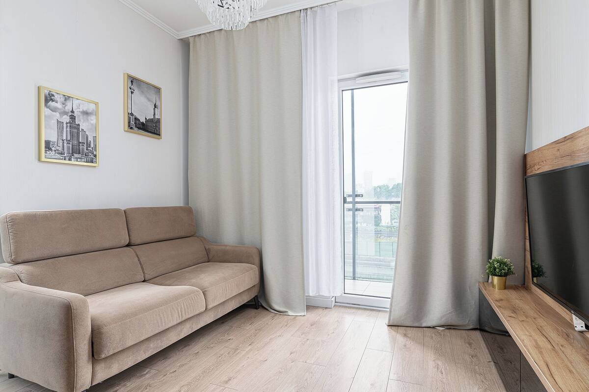 A modern living room with a beige sofa, a wooden TV stand, and two framed cityscape photographs on the wall.
