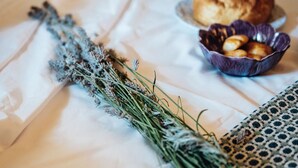 Una cama con sábana blanca, un plato de galletas y un ramo de lavanda seca.