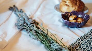 A bed with a white sheet, a bowl of cookies, and a bunch of dried lavender.