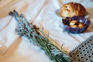A bed with a white sheet, a bowl of cookies, and a bunch of dried lavender.