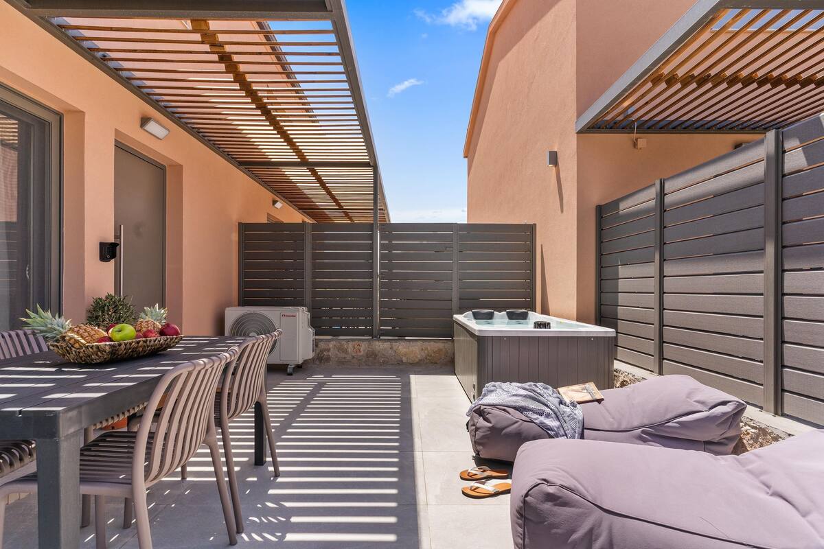 An outdoor patio with a table set for dining, a seating area with cushions, and a hot tub.