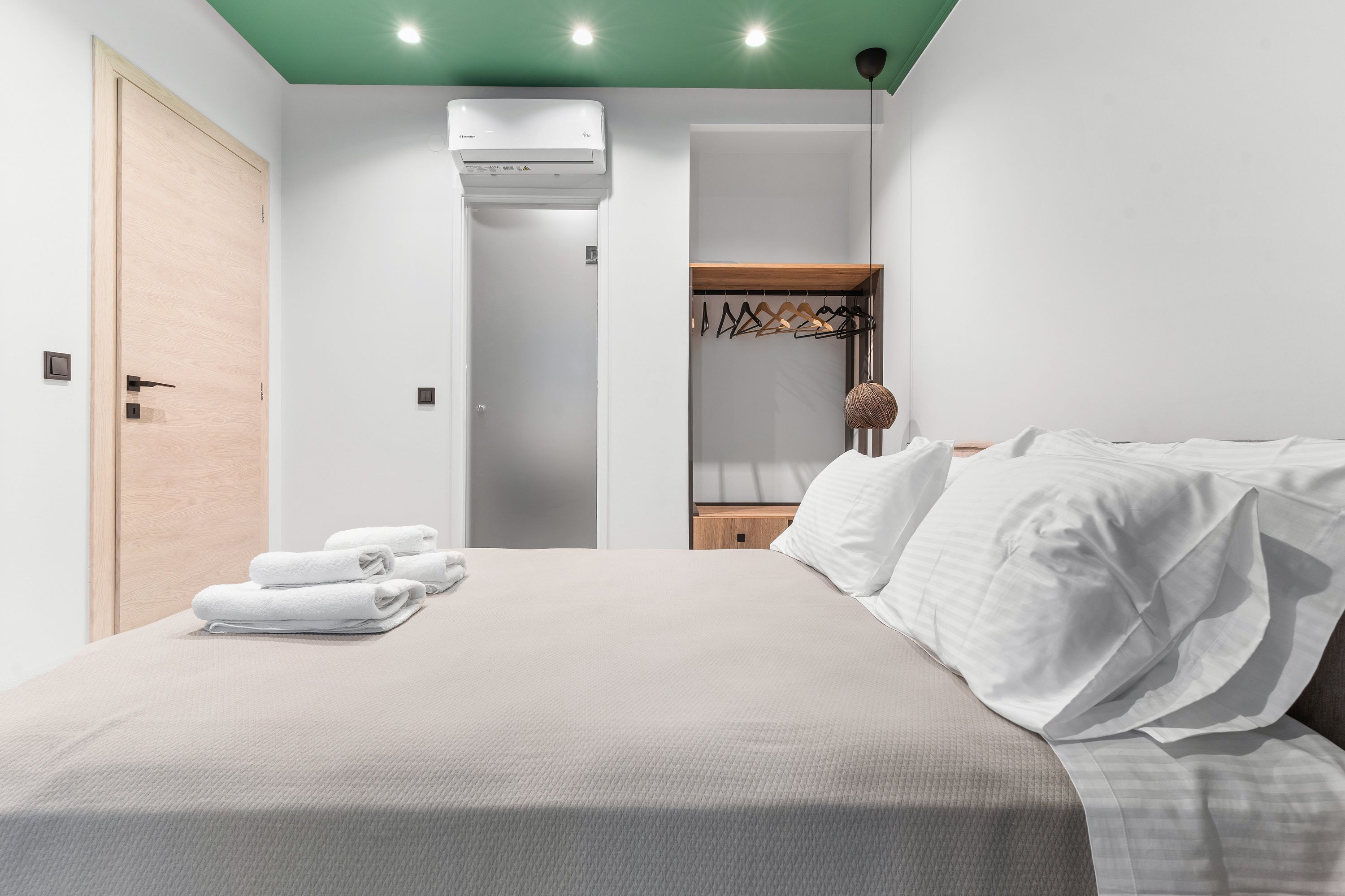A neatly made bed with white linens, a wooden door, an air conditioning unit, and a hanging light fixture.