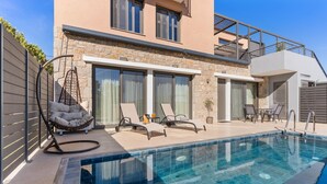 Un espace moderne aménagé au bord de la piscine, avec un mur en pierre, un fauteuil suspendu et des chaises longues.
