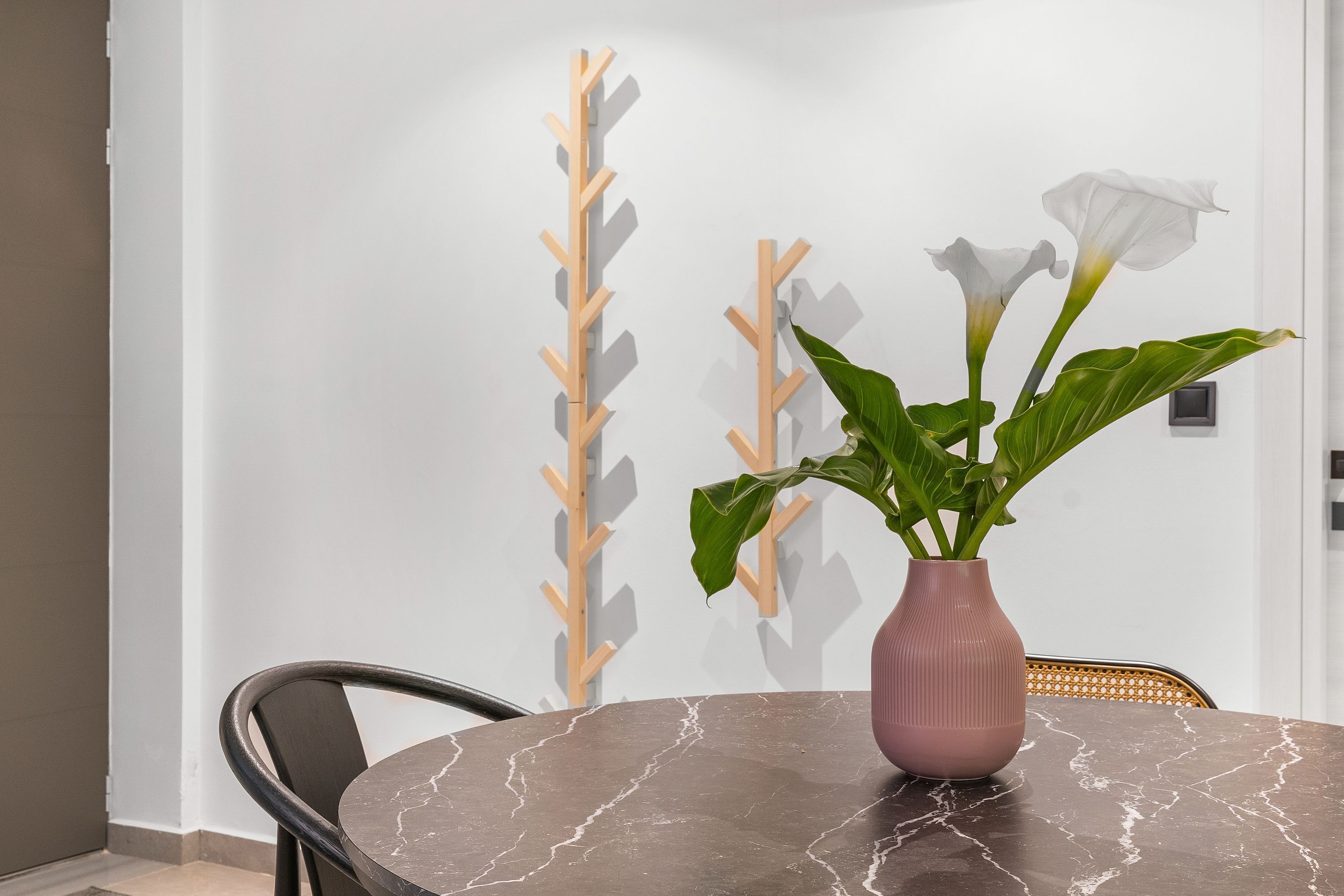 A round marble table with a pink vase containing white flowers and green leaves.