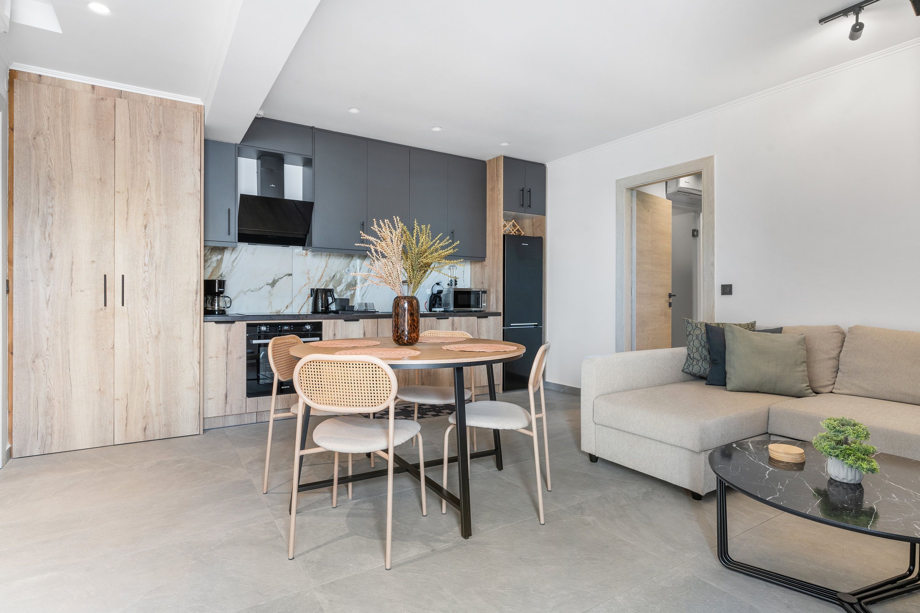 A modern kitchen with dark cabinets, a dining table with chairs, and a living area with a sofa and a coffee table.