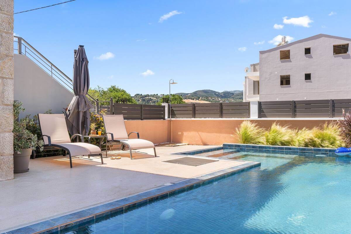 A pool area with lounge chairs, a covered seating area, and a view of the surrounding landscape.