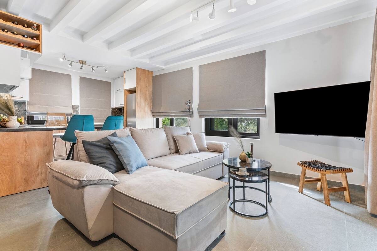 A modern living room with a sectional sofa, a small round table, and a TV mounted on the wall.