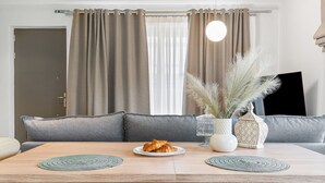 Un coin repas avec une table dressée pour deux personnes, une assiette de croissants, un vase contenant des plumes d’herbe des pampas et un chandelier.