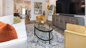 Een moderne woonkamer met een witte bank, een glazen salontafel en een grote flatscreen televisie aan de muur.