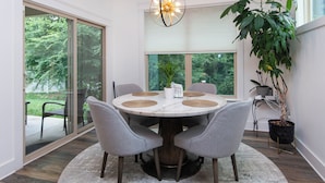 Een ronde eettafel met vier grijze stoelen, een witte vaas en een plant in een pot op de vensterbank.