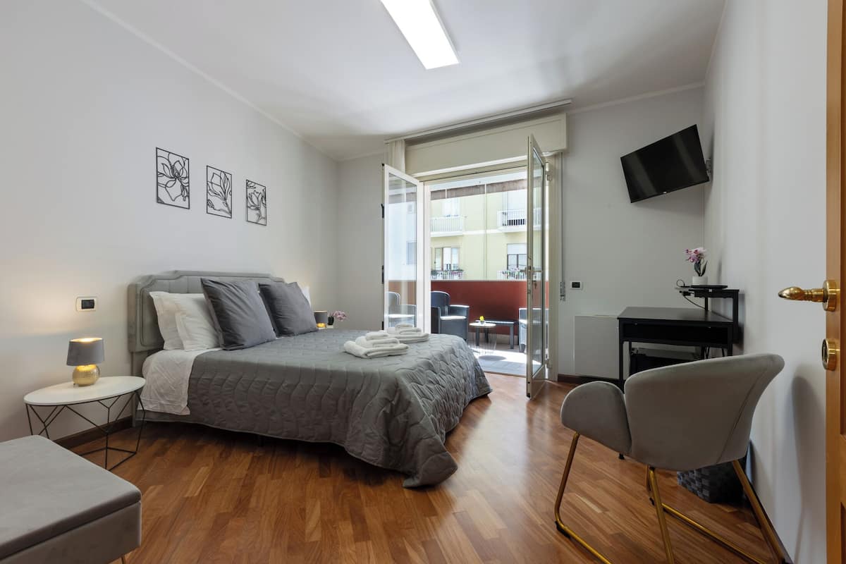 A modern bedroom with a bed, bedside table, chair, and a TV on the wall.
