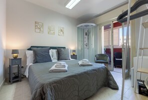 A bedroom with a bed, bedside lamps, a shower, and a chair. - Fior Di Loto Central (Cagliari)