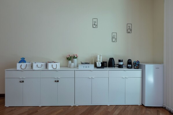 A kitchenette with a white cabinet, a coffee maker, a kettle, and a refrigerator.