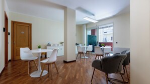 Una cocina moderna con armarios blancos, piso de madera y una zona de comedor con sillas blancas y un sofá gris.