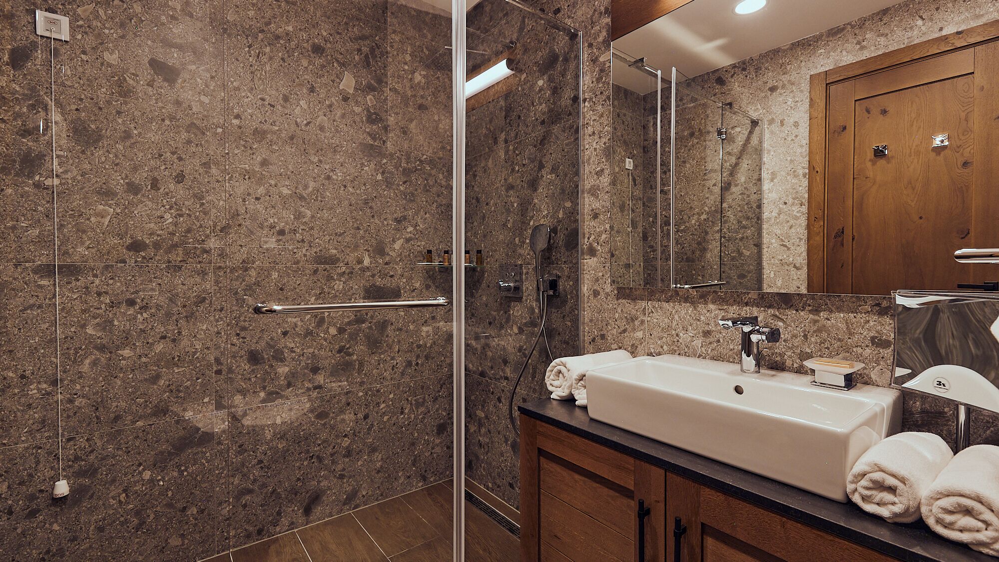 A modern bathroom with a glass-enclosed shower, a sink with a mirror, and wooden cabinets.