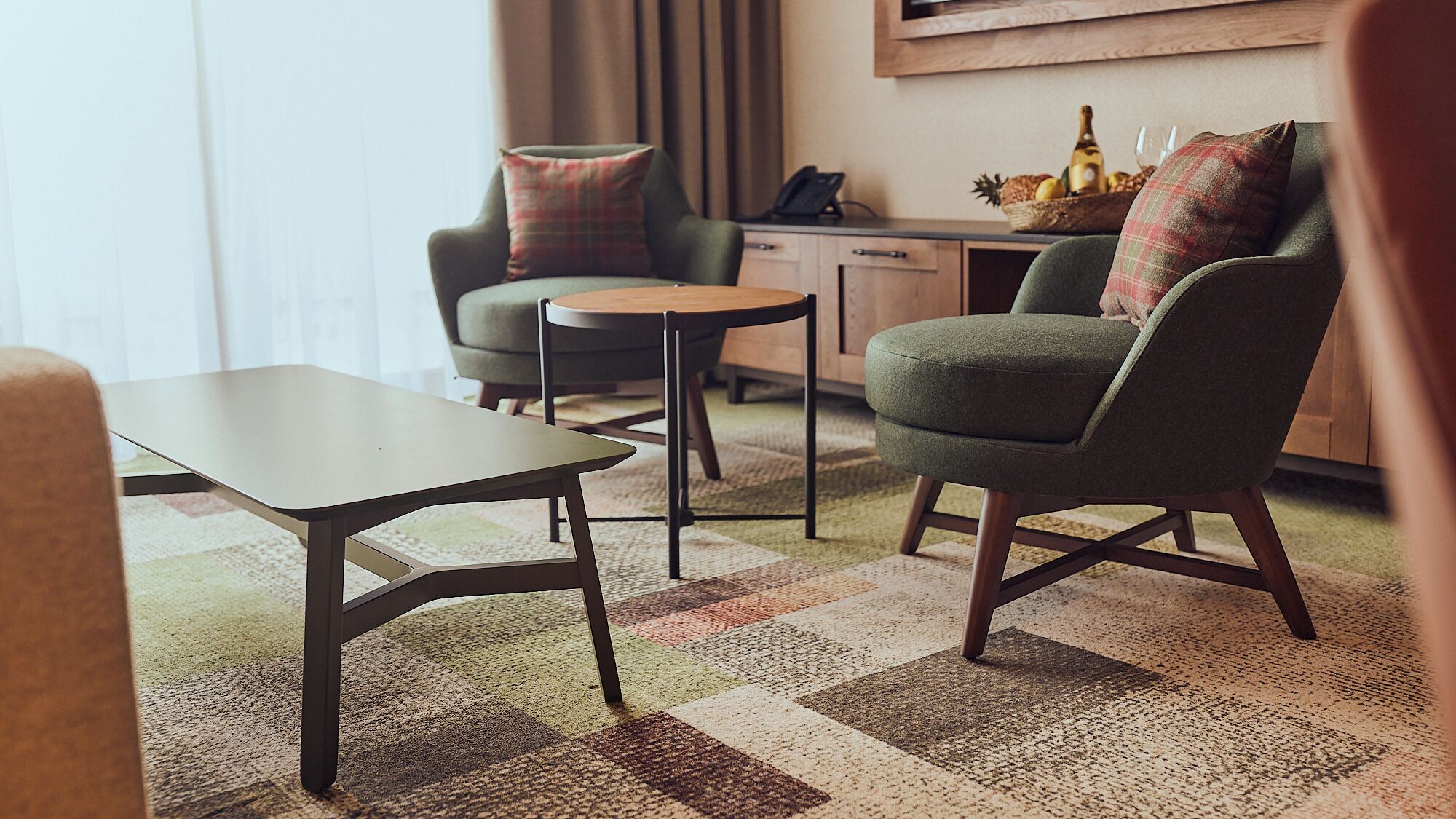 A modern living room with a sofa, a small round table, and a coffee table. There is a kitchen area with a counter and a wine bottle.