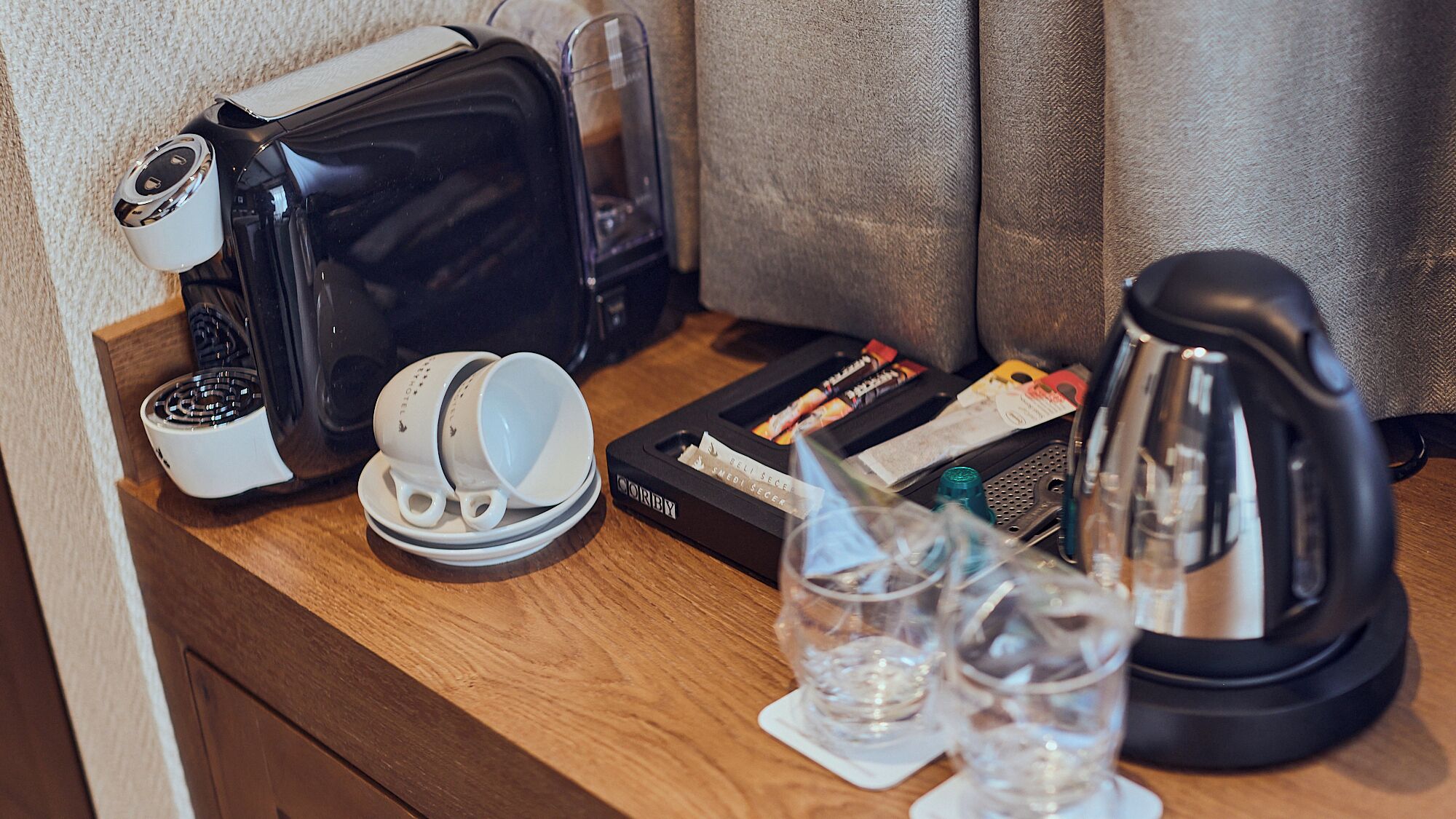 A kitchenette with a coffee maker, a kettle, a toaster, and a small glass of water on a wooden countertop.