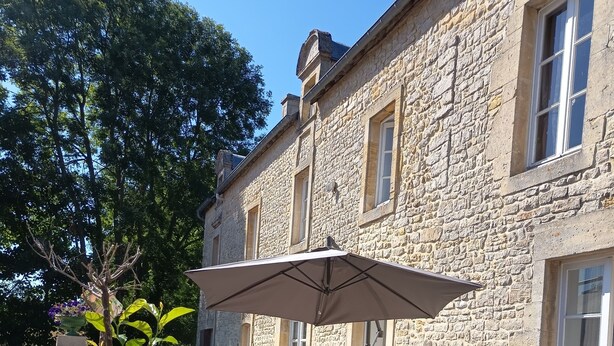 Een stenen gebouw met een terras, uitgerust met rieten meubels en een grote parasol.