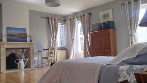 Een ruime slaapkamer met een groot bed, een houten garderobe, een open haard en een raam met gordijnen.
