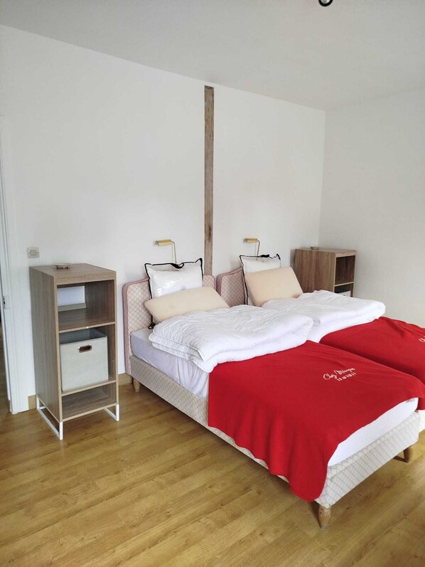 A bedroom with a bed, bedside tables, a wardrobe, and a wooden floor. - Maison de Charme La Tannerie (Tour-en-Bessin)