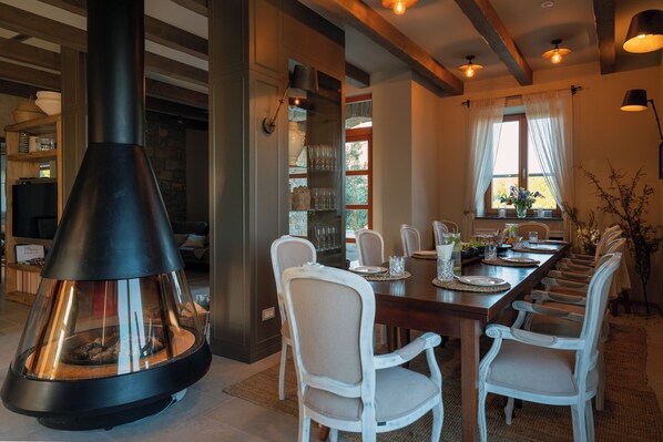 A dining area with a long wooden table, white chairs, and a black chimney.