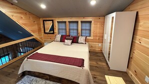 Quarto de cabana de madeira com cama, travesseiros, guarda-roupa e janela.