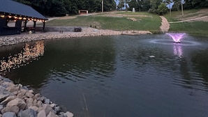 Um cenário tranquilo à beira do lago, com um coreto, uma fonte e uma área gramada bem cuidada.