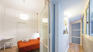 A modern bedroom with a bed, desk, chair, and a hallway leading to a bathroom. - Lioy 25 by Napoliapartments (Naples)