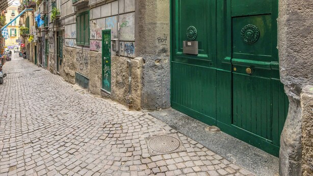 A cobblestone street with a green door and a stone archway. - Lioy 25 by Napoliapartments (Naples)