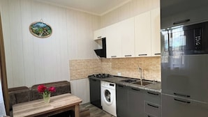 A compact kitchen with a built-in washer, a dining area with a bench, and a wall-mounted artwork. - Royal Galaxy

 (Stepantsminda)