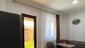 A compact living space with a kitchenette, a dining area with a wooden table and bench, and a sliding glass door leading to a garden. - Royal Galaxy

 (Stepantsminda)