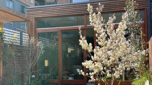 Een modern gebouw met grote glasramen en een verzorgde tuin met bloeiende planten.