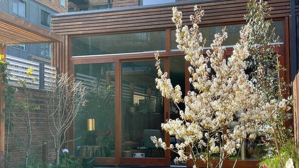 A modern building with large glass windows and a well-maintained garden with flowering plants. - A minute to the tram, a minute to the beach-explore Amsterdam like never before (Amsterdam)
