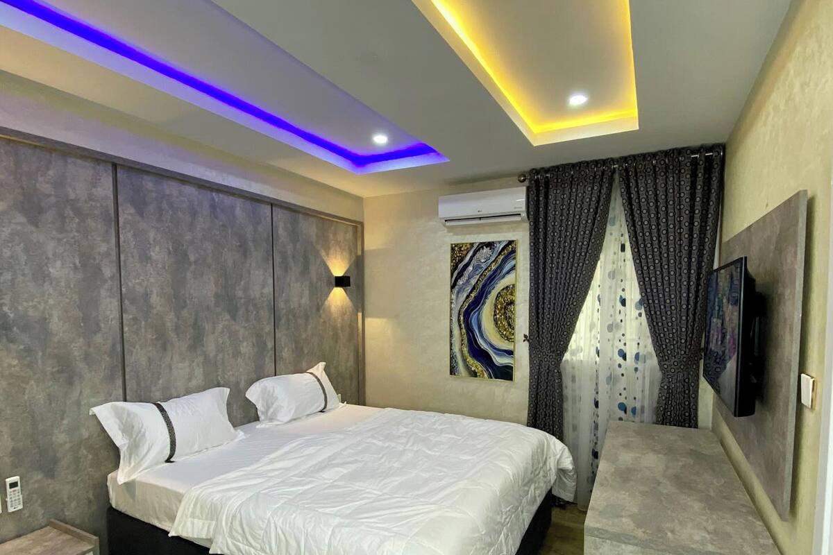 A modern bedroom with a bed, bedside tables, a TV, and a ceiling with LED lighting.