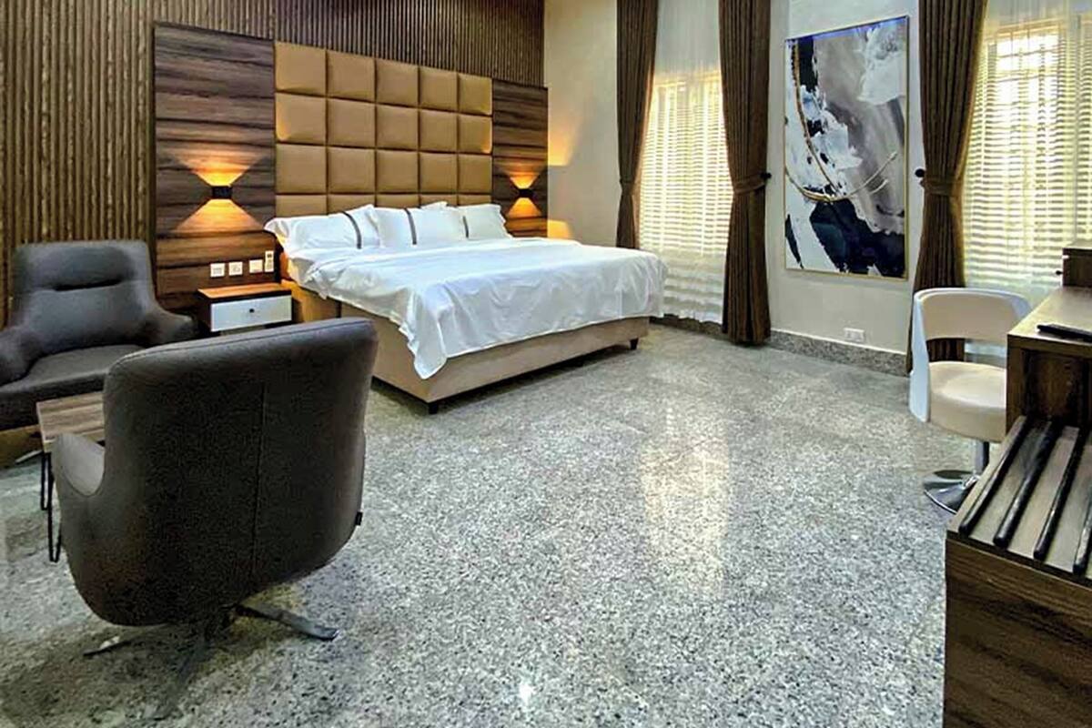 A modern hotel room with a large bed, a desk, a chair, and a sofa.