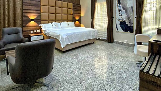 A modern hotel room with a large bed, a desk, a chair, and a sofa.